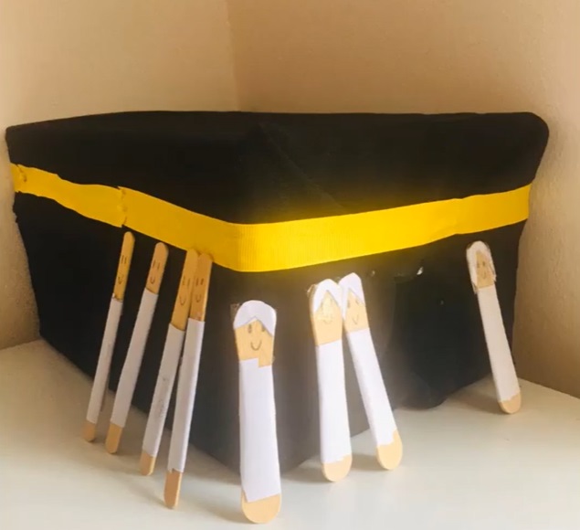 A handmade model of the Kaaba with a yellow band and craft-stick figures